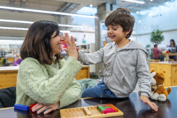 Mother and young boy high fiving, sharing a moment of success and happiness while playing a wooden puzzle game together on a table in an indoor learning environment