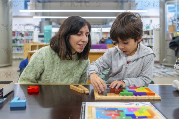 Woman and boy are playing with a colorful wooden tangram puzzle, focusing on solving the geometric shapes for an engaging and stimulating educational activity in an indoor setting