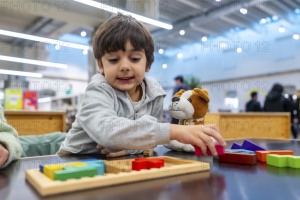 Young boy concentrating as he arranges colorful wooden puzzle pieces beside a soft toy dog, demonstrating early learning, fine motor skills and playful problem solving development