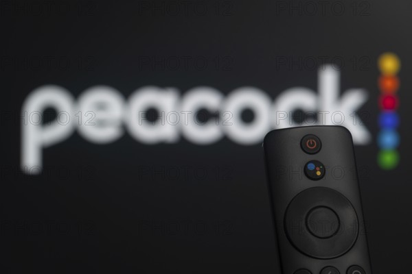 Dhaka, Bangladesh- 21 Jan 2026: Close-up of a smart TV remote control against a blurred peacock logo