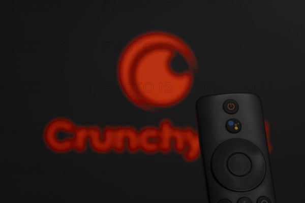 Dhaka, Bangladesh- 21 Jan 2026: Close-up of a smart TV remote control against a blurred Crunchyroll logo