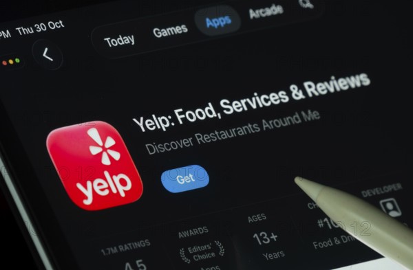 Dhaka, Bangladesh- 30 Oct 2025: Yelp app displayed on a iPad screen in dark mode with a digital pen pointing at it