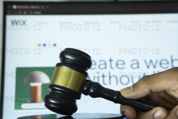 Dhaka, Bangladesh- 20 June 2025: A hand holds a gavel in front of a computer screen displaying Wix's website
