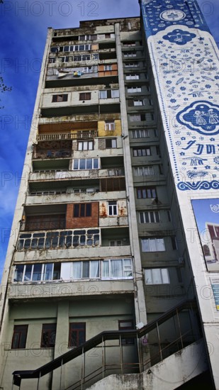 The colorful façade with windows, balconies, laundry, of a tall, old, partly dilapidated residential building, nostalgic charm, against a cloudy sky, Georgia