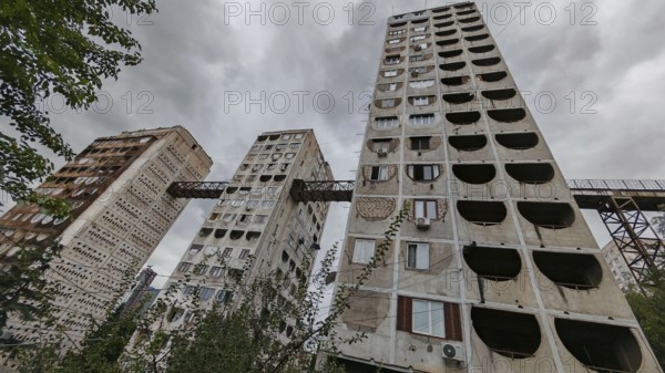 Three high-rise buildings connected by metal bridges under cloudy skies, nostalgic charm, architecturally interesting living silo, prefabricated buildings, Tbilisi, Georgia