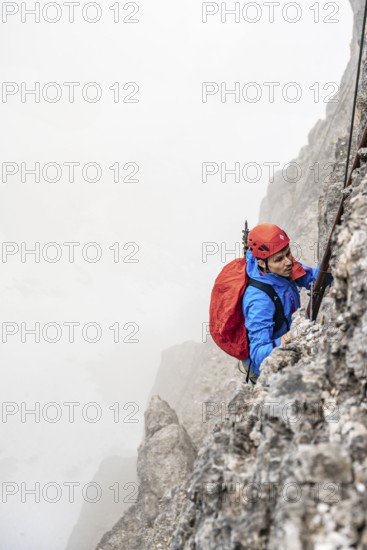 Mountaineers on a ladder on the Via Ferrata Oliva Detassis via ferrata in fog, rocky mountain peaks and mountain landscape, Brenta Mountains, Parco Naturale Brenta-Adamello, Trentino, Italy