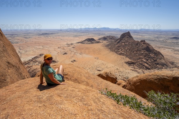 Woman sitting on rocks and enjoying the view over the barren desert landscape of Spitzkoppe, Spitzkoppe, Erongo, Namibia