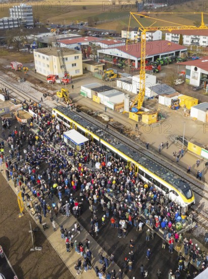Large crowd in front of a train on a construction site, aerial view with crane in the background, opening of the Hermann Hesse Railway, Calw, Germany