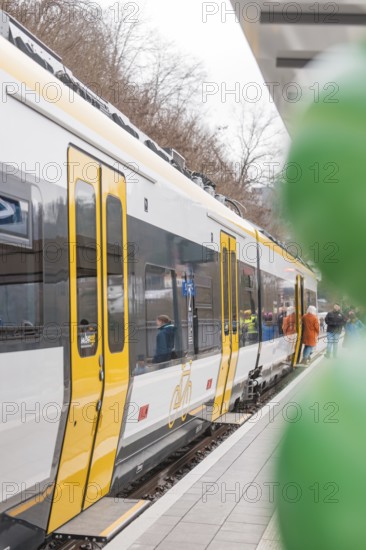 A yellow and white train stands on the platform with people and green balloons, opening of the Hermann Hesse Railway, Calw, Germany