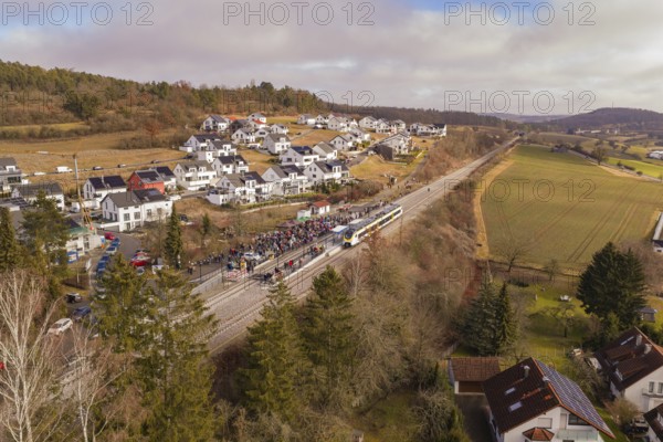 Aerial view of a rural village with a crowd of people on a railroad track, surrounded by hills and fields, opening of the Hermann Hesse Railway, Calw, Germany