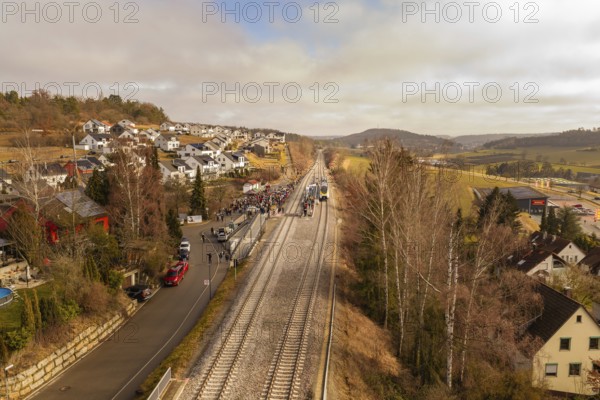 A railway line runs through a village with houses and trees in a hilly winter landscape, opening of the Hermann Hesse Railway, Calw, Germany