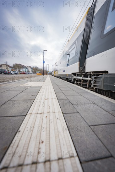 View along an empty sidewalk at a train station under a grey sky, opening of the Hermann Hesse Railway, Calw, Germany
