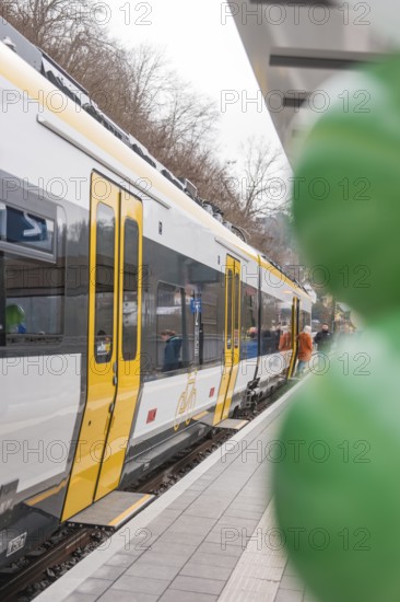 Yellow and white train on a platform with colorful balloons in the foreground, opening of the Hermann Hesse Railway, Calw, Germany