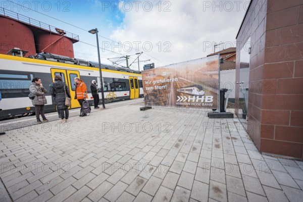 People wait on the railroad track next to a yellow train, a large poster is visible, battery electric train Siemens Micro Plus B, Hermann, Hesse, Bahn, Weil der Stadt, Böblingen district, Germany