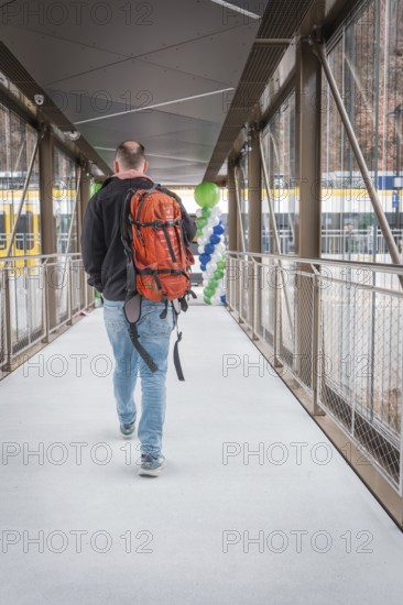 Man with orange backpack walks across a glazed transition with balloons, battery electric train Siemens Micro Plus B, Hermann, Hesse, Bahn, Weil der Stadt, Böblingen district, Germany