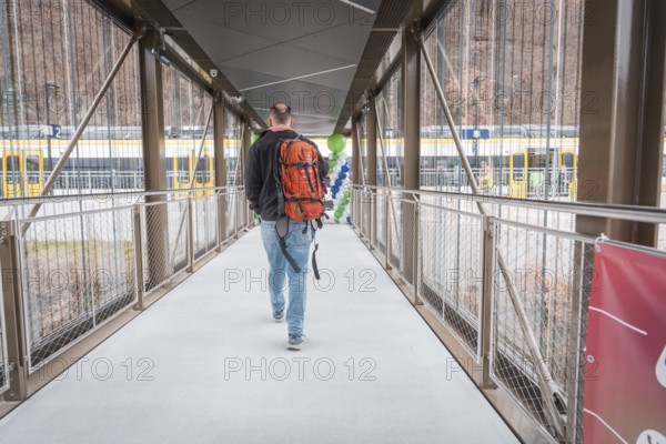 Man with backpack walking across bridge, yellow train in background, battery electric train Siemens Micro Plus B, Hermann, Hesse, Bahn, Weil der Stadt, Böblingen district, Germany