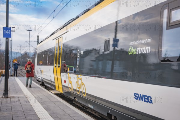 A SWEG train with green energy branding stands at the station while a person with a backpack passes by, battery electric train Siemens Micro Plus B, Hermann, Hesse, Bahn, Weil der Stadt, Böblingen district, Germany