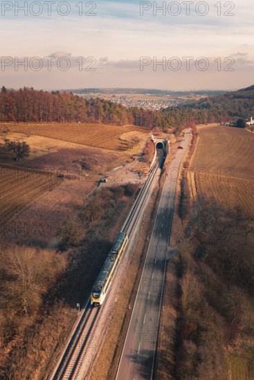 A train travels on rails parallel to a country road at a tunnel in a scenic area, fire drill on the Hermann Hesse Railway, Ostelsheim, Germany