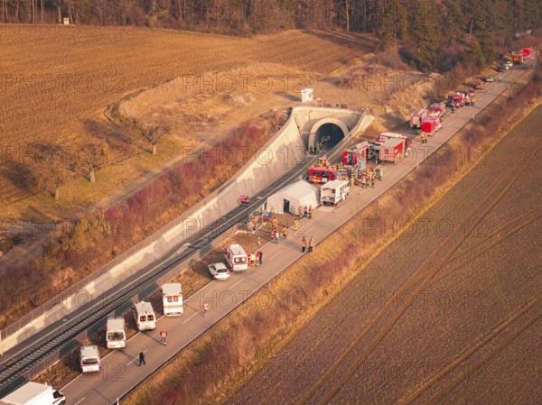Fire engines and rescue workers in front of a tunnel in a rural area at sunset, fire drill on the Hermann-Hesse railway, Ostelsheim, Germany