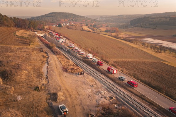 Fire trucks on a country road next to railroad tracks at sunset in a hilly landscape, fire drill on the Hermann Hesse Railway, Ostelsheim, Germany