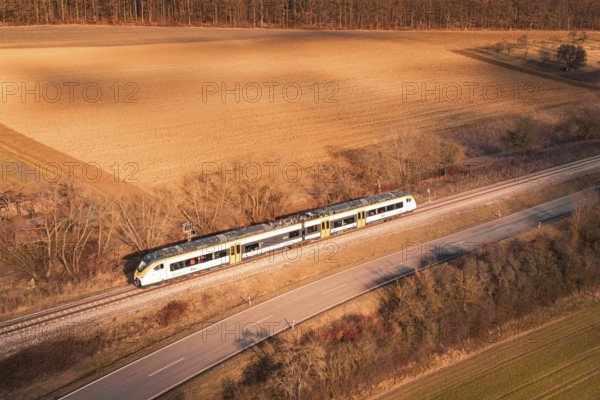 Train travels along railroad tracks between fields and forest at sunset, fire drill on the Hermann-Hesse railway, Ostelsheim, Germany