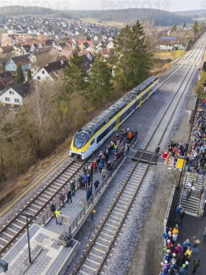 A train stops at a platform surrounded by a crowd of people. In the background you can see a village and wooded hills, opening of the Hermann Hesse Railway, Calw, Germany