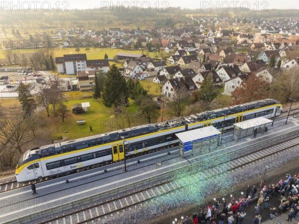 A train is standing at a train station, people are standing to the right, a village and fields in the distance, opening of the Hermann Hesse Railway, Calw, Germany