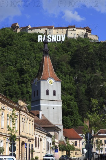 Town of Rasnov, German Rosenau. In the foreground is the distinctive clock tower of the Protestant Church, St. Matthias Church, in the background on the hill is the medieval Rasnov Fortress, Rosenau Castle, Brasov District, Transylvania, Romania