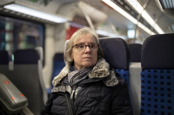 Elderly woman, portrait, thoughtful, glasses, gray hair, coat, scarf, winter clothes, sitting in the S-Bahn, Stuttgart, Baden-Württemberg, Germany