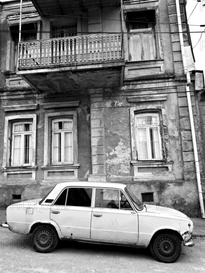 Monochrome, vintage car standing in front of a Nostaligian building with a distinctive balcony, Georgia
