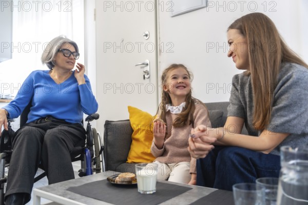 Loving three generation familygrandmother in wheelchair, mother and young daughter sharing smiles, conversation and gentle care during a warm, relaxed visit at home