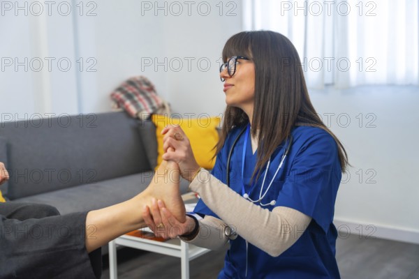 Healthcare professional wearing blue scrubs and a stethoscope examining an elderly patient's foot and ankle, providing physical therapy and rehabilitation in a comfortable home setting