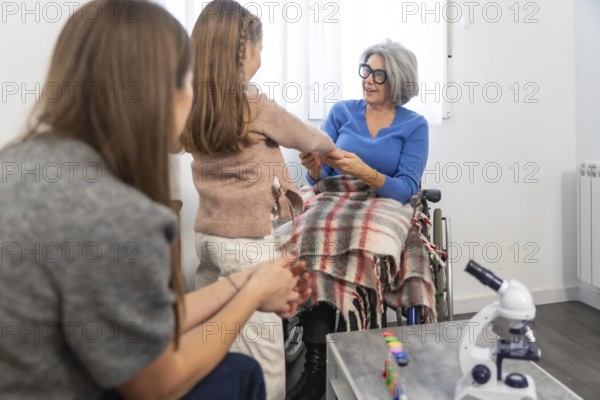 Family members, including a young girl and her mother, are visiting an elderly grandmother in a wheelchair, holding hands and sharing a moment of intergenerational connection and care