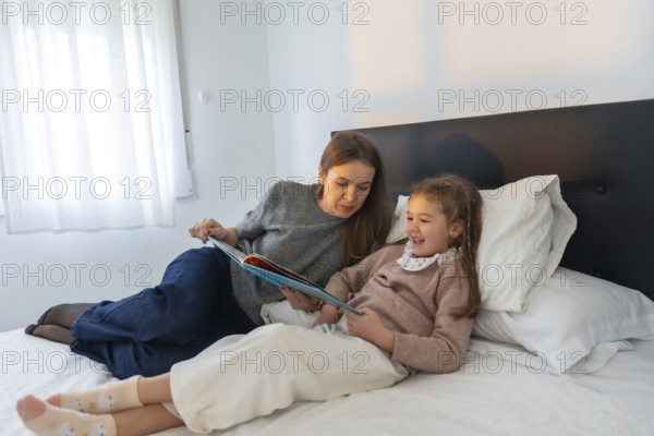 Mother and young daughter bonding over a book in bed, sharing a laugh and enjoying quality time while reading a story at home, fostering literacy and family connection
