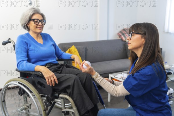 Caregiver working with a senior woman in a wheelchair, providing assistance and support during rehabilitation exercises with a small ball, highlighting concepts of elderly care and physical therapy
