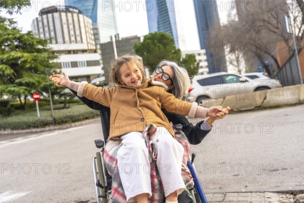 Smiling granddaughter sitting on grandmothers lap in a wheelchair as they enjoy an outdoor stroll together near a city nursing home, sharing laughter, love and support