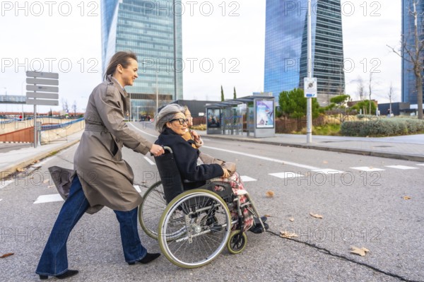 Daughter pushing a happy elderly woman in a wheelchair, moving along a modern city street with skyscrapers in the background, enjoying a walk together