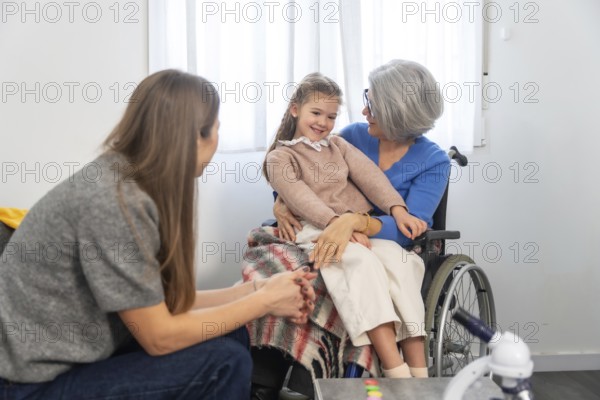 Family members connecting during a visit, with a smiling granddaughter sitting comfortably on her grandmother's lap in a wheelchair, symbolizing love and intergenerational bonds