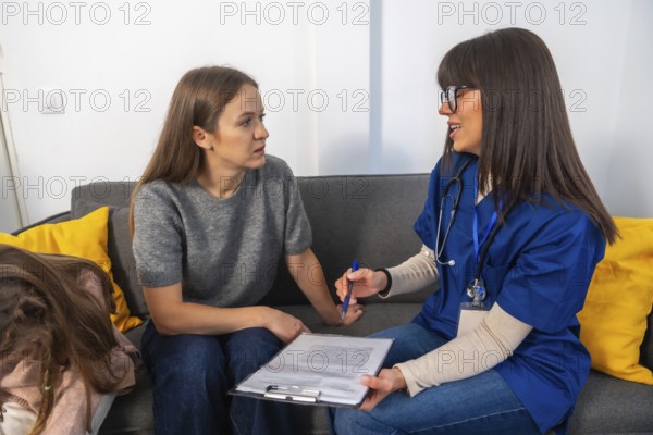 Nurse in scrubs with stethoscope consults a woman at home, explaining medical options and paperwork while offering supportive elder care advice in a living room setting
