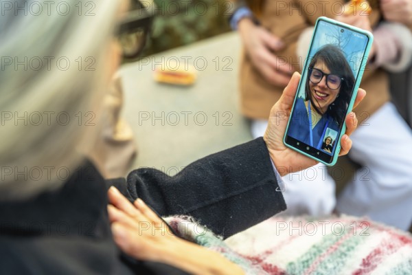 Senior woman in a wheelchair having a video call with a younger family member on a smartphone while enjoying an outdoor walk, staying connected with loved ones using technology
