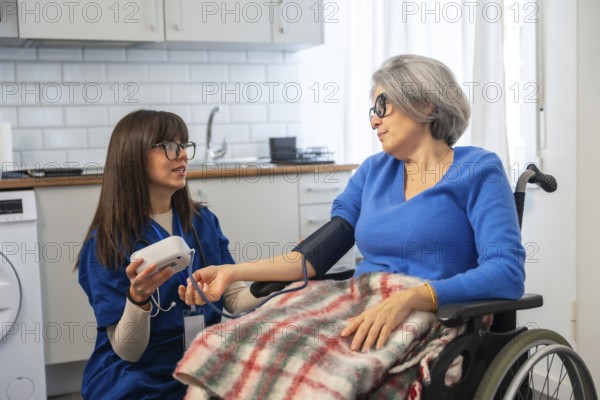 Healthcare professional assisting an elderly woman in a wheelchair by measuring her blood pressure at home, providing medical care and support for independent living