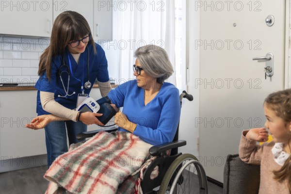 Healthcare professional assisting an elderly woman in a wheelchair by measuring her blood pressure with an automatic monitor during a home visit, emphasizing elder care and medical support