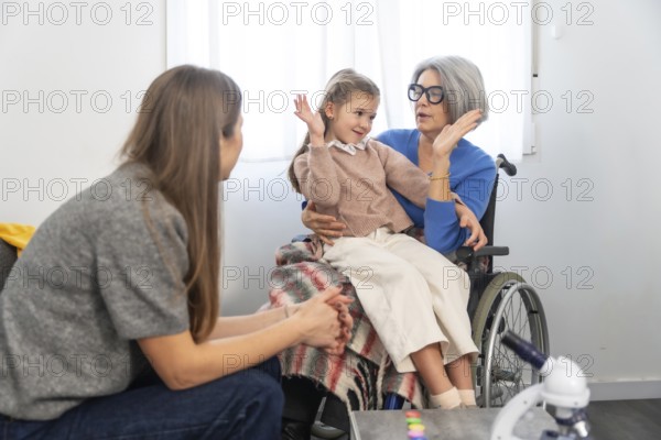 Family members connecting during a visit, with a senior woman in a wheelchair holding her granddaughter on her lap while talking, fostering intergenerational bonds and care