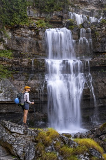 Young pretty hiker standing on rocks in front of Cascata di Mezzo waterfall, long exposure, Vallesinella, Brenta, Trentino, Italy