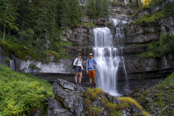 Two hikers standing on rocks in front of Cascata di Mezzo waterfall, long exposure, Vallesinella, Brenta, Trentino, Italy