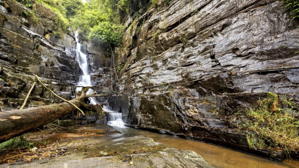 A narrow waterfall flows in a rough environment from rocks surrounded by forest, waterfall in the mountains of Kandy in Sri Lanka