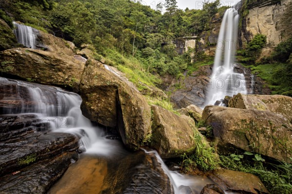 Two waterfalls flow between large rocks in a lush, green jungle, waterfall in the mountains of Kandy in Sri Lanka