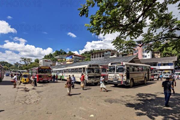 Busy bus stop with people and buses under a sunny sky with green trees, Kandy bus station in Sri Lanka