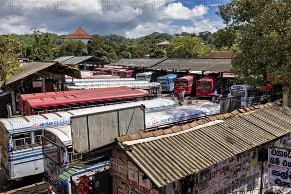 View of a bus depot with numerous parked buses and green hills in the background, Kandy bus station in Sri Lanka