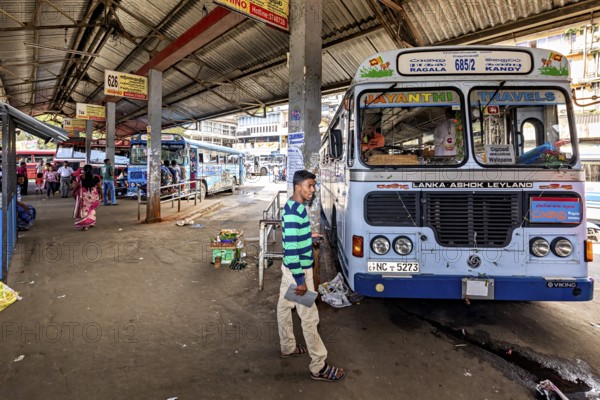 A bus station with parked buses and people walking between the covered stops, Kandy bus station in Sri Lanka